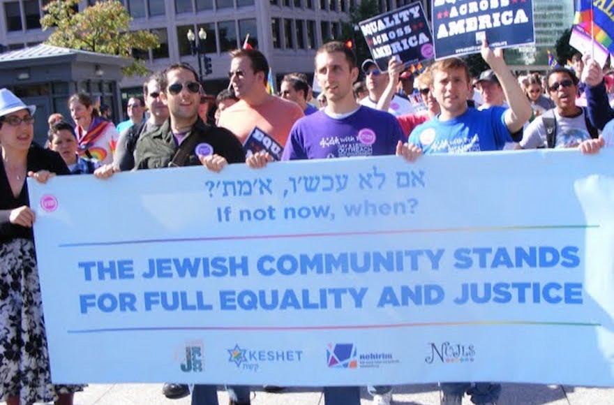 Image is of people marching in the streets. Four people in the front are carrying a banner that says The Jewish community stands for full equality and justice.