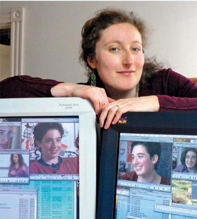 Image of Irena Fayngold standing with her arms on top of two computers showing images from "Hineini."