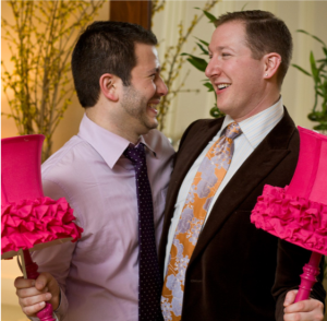 Image of Steven Davis and J. Jacob Krause smiling at each other. They are wearing suits and are holding pink decorations.