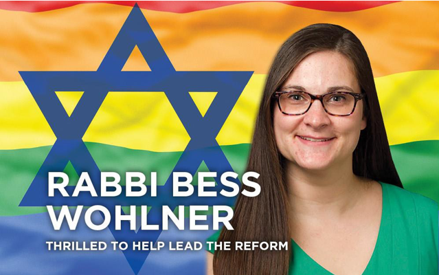 Image of Rabbi Bess Wohlner in front of a rainbow LGBTQ flag, with a Blue Star of David. White text reads: "Rabbi Bess Wohlner: Thrilled to Help Lead the Reform."