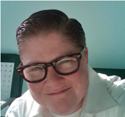 Image of Sasha T. Goldberg wearing glasses and smiling in front of a blue wall.