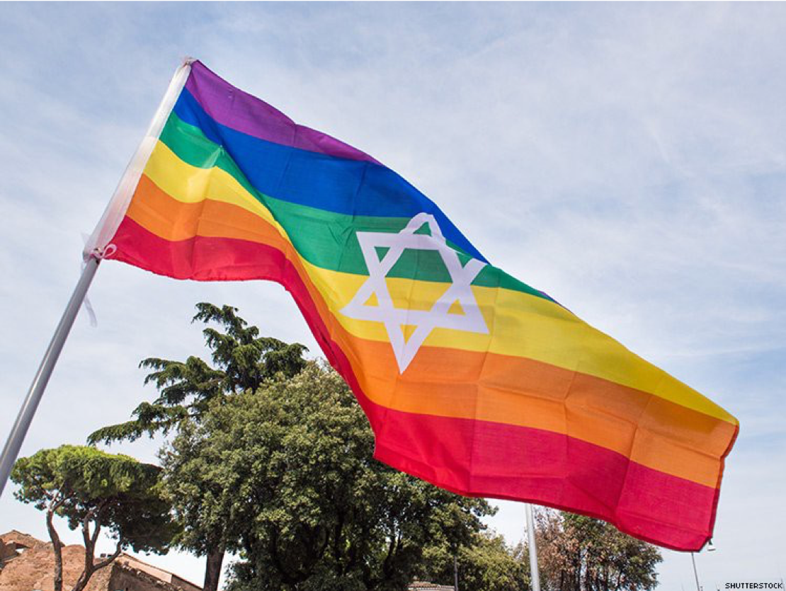 Image of a large rainbow LGBTQ flag with a Star of David on it flying outside.