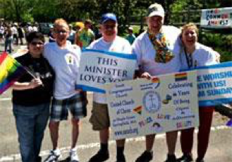 Image of a group of five people holding signs and rainbow flags. One sign reads: "This minister loves you."