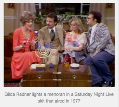 Image of Gilda Radner lighting a menorah. She is sitting on a couch with three other people who are watching her.