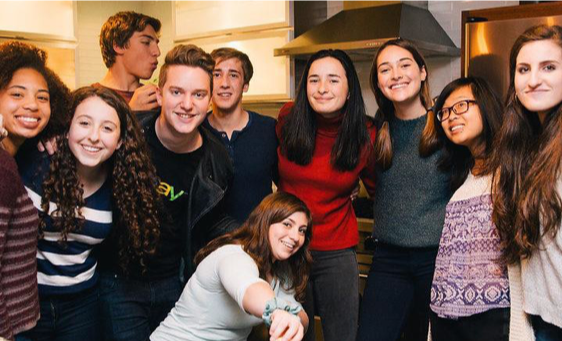 A group of teens with their arms around each other, smiling at the camera.