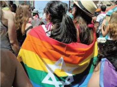 Image of two people wrapped in a rainbow flag with the Star of David on it at a Tel Aviv Pride Parade.