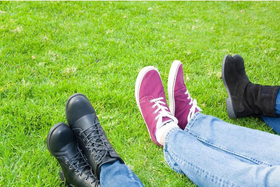 Image of three people's shoes on top of grass.