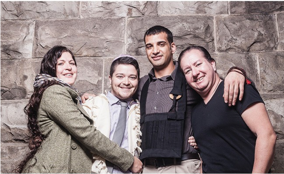 Image of four people standing with their arms around each other in front of a brick wall. Rafi Daugherty is the second person.