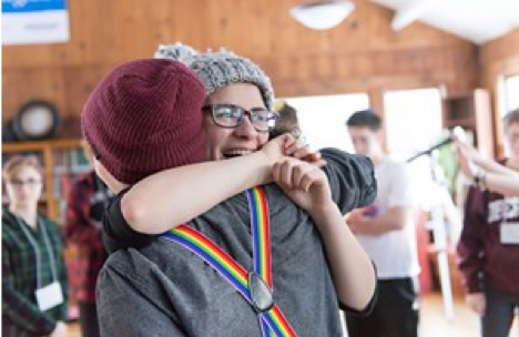 Image of two teens hugging. One is wearing rainbow suspender straps.