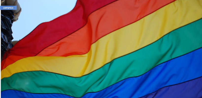 Image of a large rainbow LGBTQ flag flying outside.