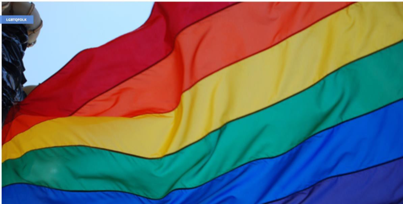 Image of a large rainbow LGBTQ flag flying outside.