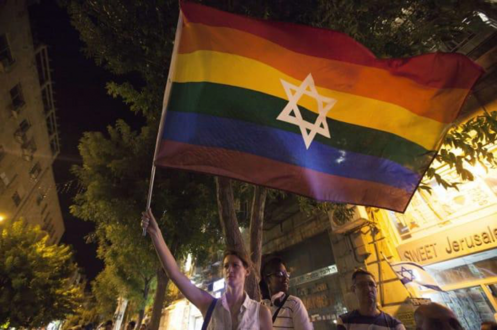Image of a woman holding a rainbow LGBTQ flag with the Star of David on it.