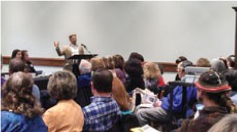 Image of a group of people watching a person speak .