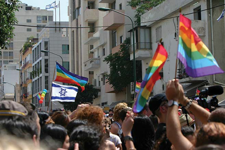 Image of a Pride Parade with several rainbow LGBTQ flags and one Israeli flag.