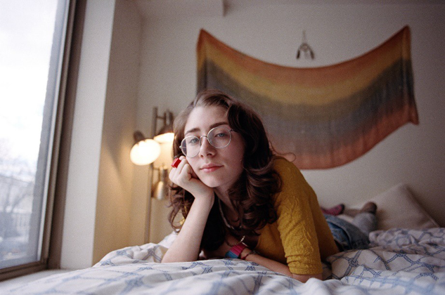 Image of Milah Carlone lying on a bed with a rainbow Pride flag visible in the background.