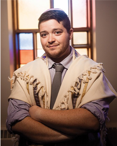 Image of Rafi Daugherty. He is wearing a button-down shirt and tie, and a kippah. He is standing with his arms crossed in front of a window.