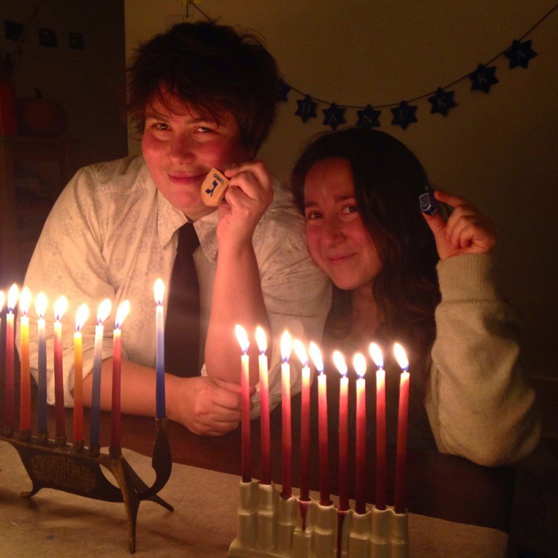 Image of Vanessa and anther person sitting in front of two lit menorahs.