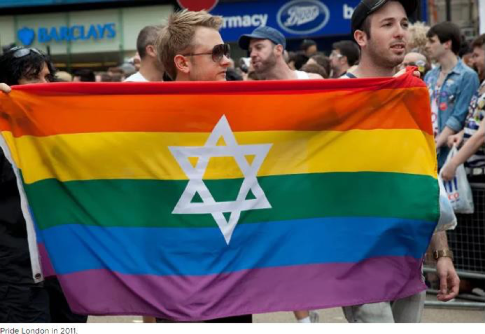 Image of several people carrying a rainbow LGBTQ flag with a Star of David on it in a Pride Parade.