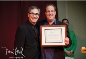 Image of two people standing together smiling. The person on the right is holding a framed certificate.