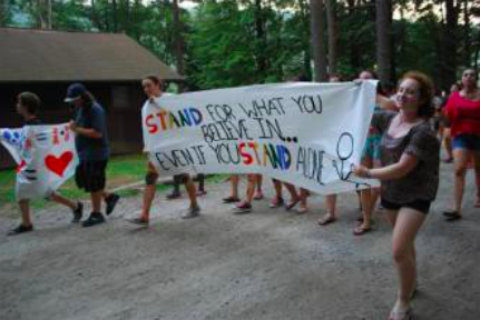 An image of the campers marching with a giant banner that reads: "Stand for what you believe in... even if you stand alone."