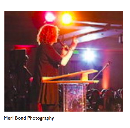 Image of Judy Gold standing on a stage holding a microphone.