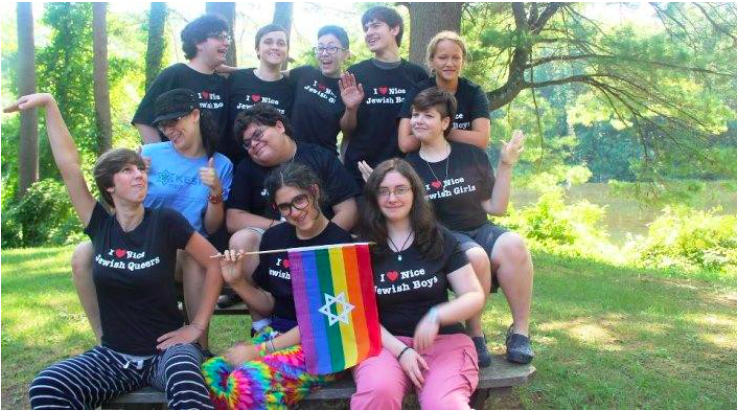 Image of a group of teens sitting together outside. They are smiling and laughing, and all wearing black shirts that read: "I heart nice Jewish girls/boys/queers"