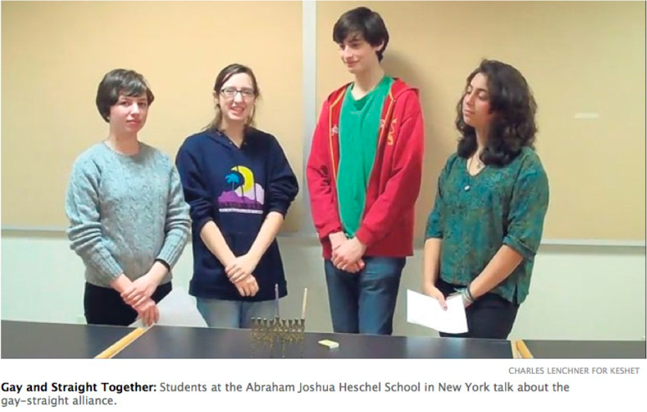 Image of four students standing together in a classroom. An menorah is on the table in front of them.