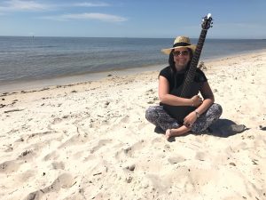 Rabbi Alexis Pinsky sitting on the beach, holding a guitar.