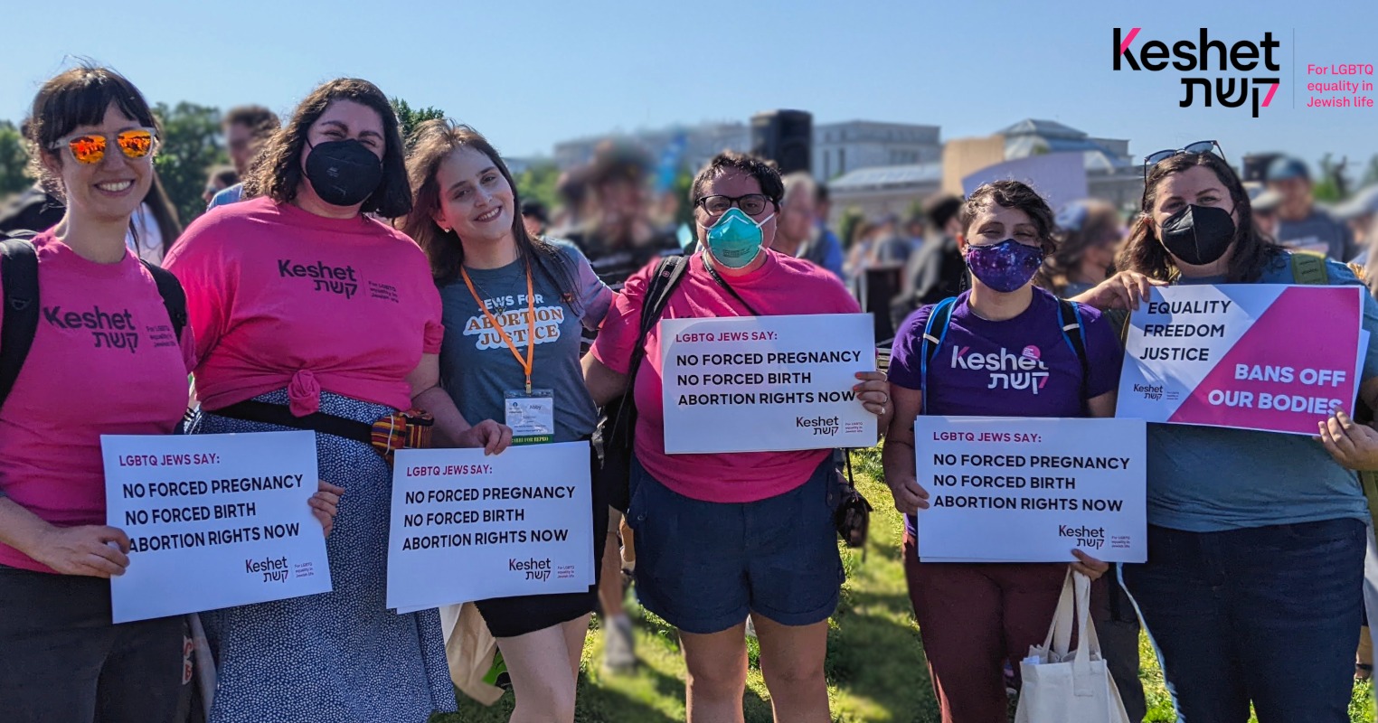 6 people standing outside at a sunny political rally, wearing Keshet t-shirts and holding signs that say "No Forced Pregnancy, No Forced Birth, Abortion Rights Now"
