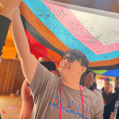 A teenage student holds an LGBTQ+ pride flag up and smiles